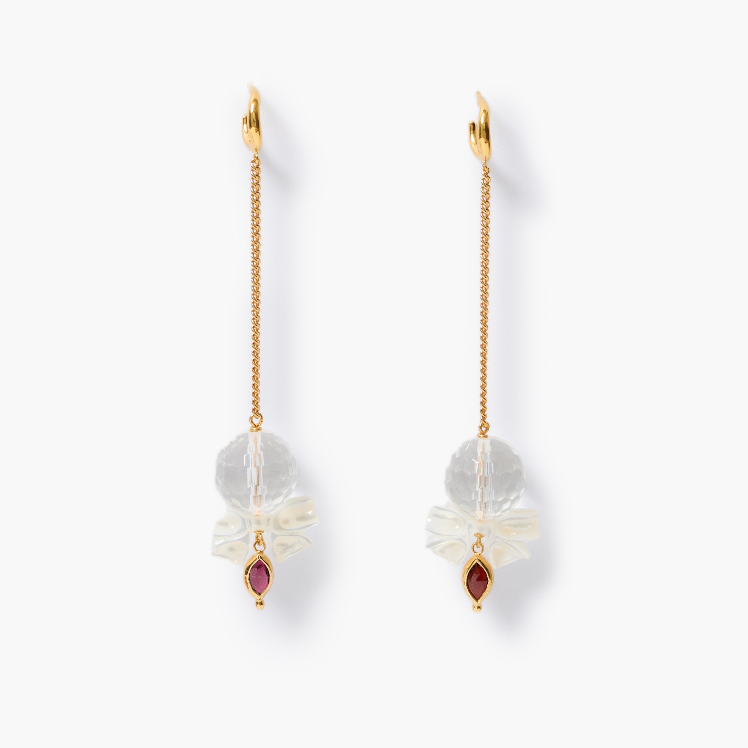A pair of gold dangle earrings with white mother-of-pearl bow charms with faceted clear quartz spheres and small bezeled lens-shaped garnet gemstones, shown on a clean white background.