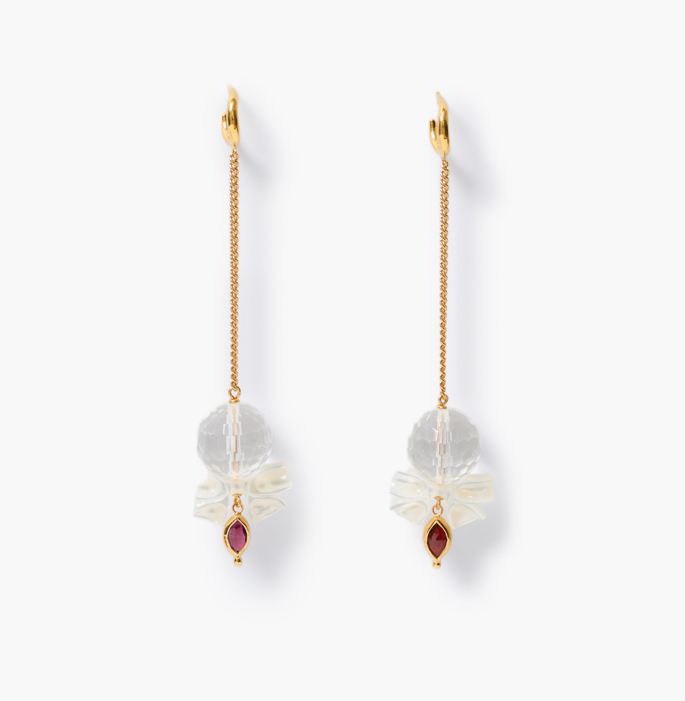 A pair of gold dangle earrings with white mother-of-pearl bow charms with faceted clear quartz spheres and small bezeled lens-shaped garnet gemstones, shown on a clean white background.